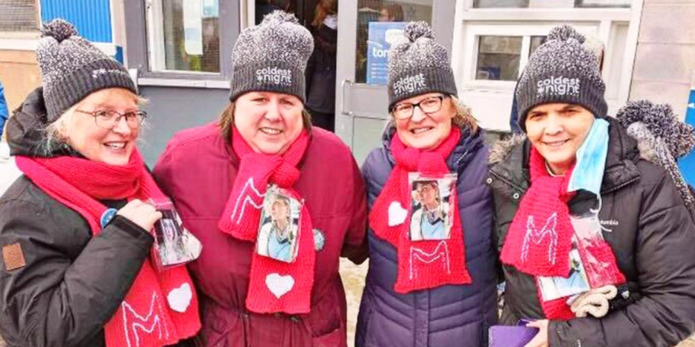 Four women wearing greay toques and red scarves